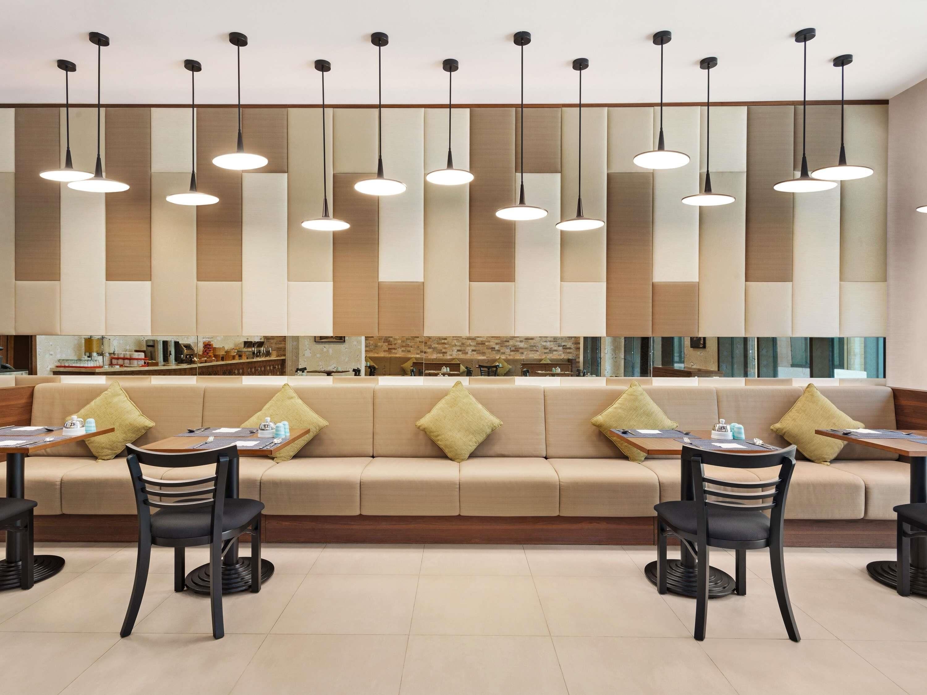 Un comedor moderno con sofá y mesas, iluminación colgante y una cocina al fondo.