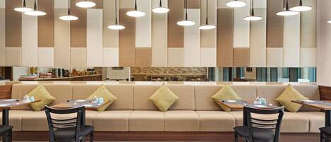 Un comedor moderno con sofá y mesas, iluminación colgante y una cocina al fondo.