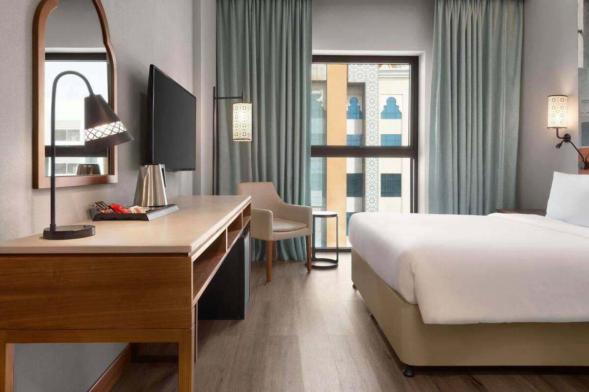 Ein Hotelzimmer mit einem Bett, einem Schreibtisch mit Stuhl, einem Fernseher und einem Fenster mit Vorhängen.