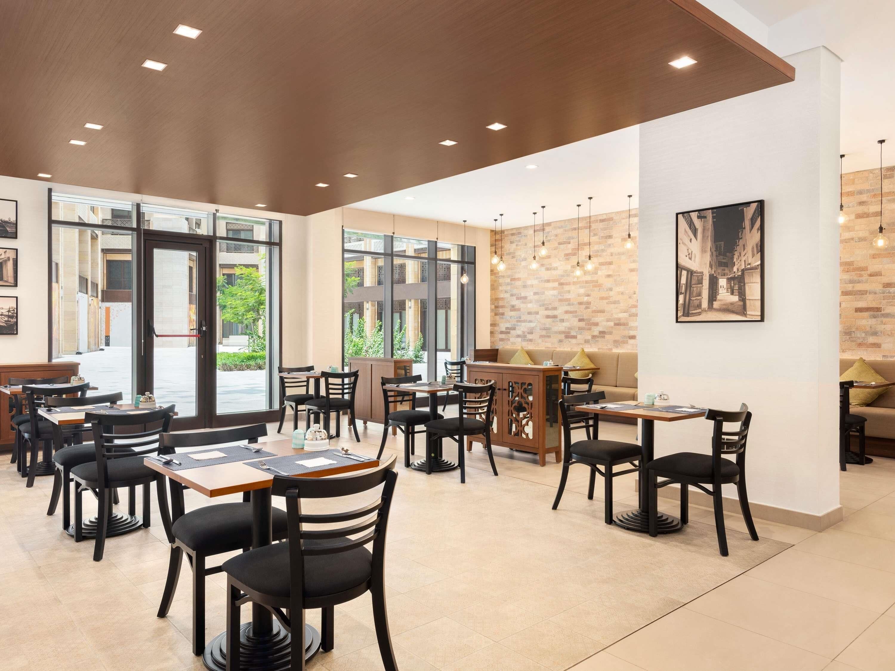 Un café spacieux avec de nombreuses tables et chaises, de grandes fenêtres et un mur en briques.