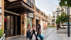 A modern building with a glass entrance, a metal balcony, and a paved walkway.