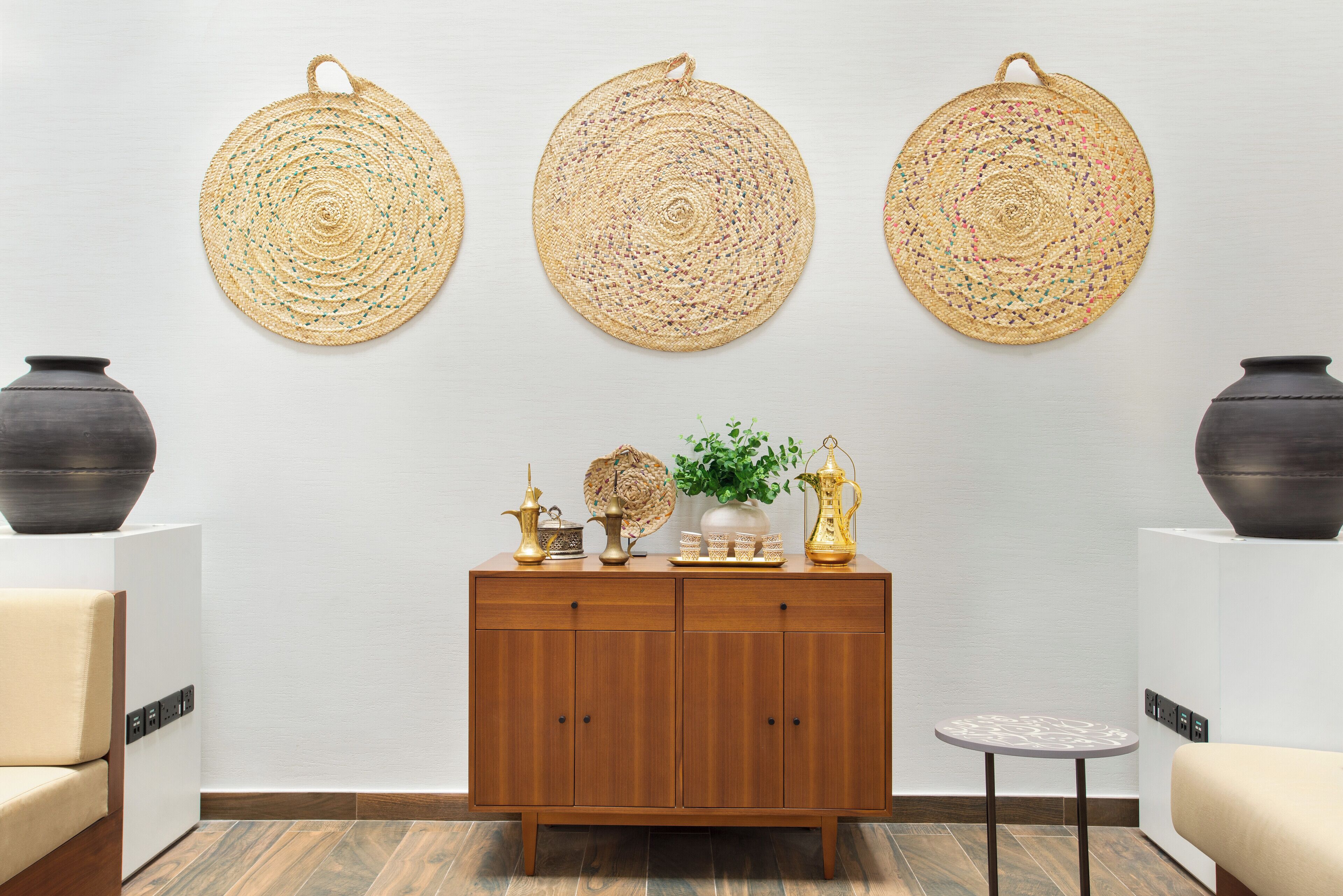 A modern room with a wooden cabinet, three woven wall hangings, and two vases on the cabinet.