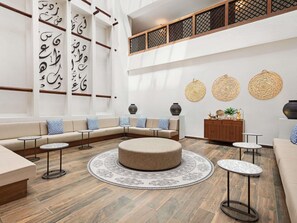 Un espace salon moderne avec un canapé d’angle, un pouf rond et de petites tables.
