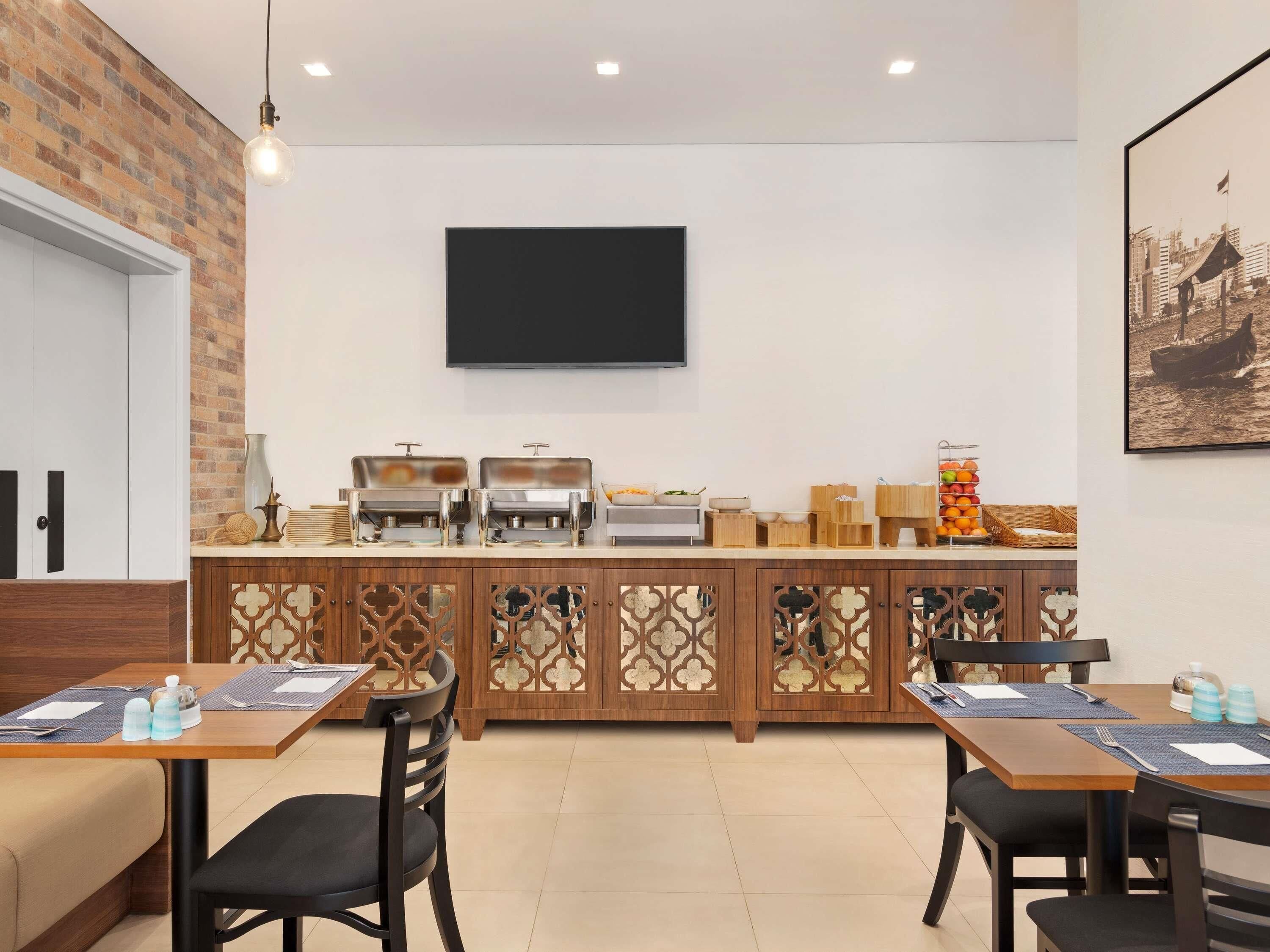 A modern dining area with a buffet setup, a flat-screen TV mounted on the wall, and a seating arrangement with tables and chairs.