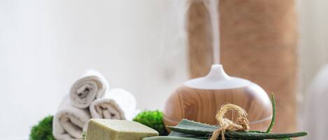 A wooden cutting board with soap, aloe vera, and a rolled towel.