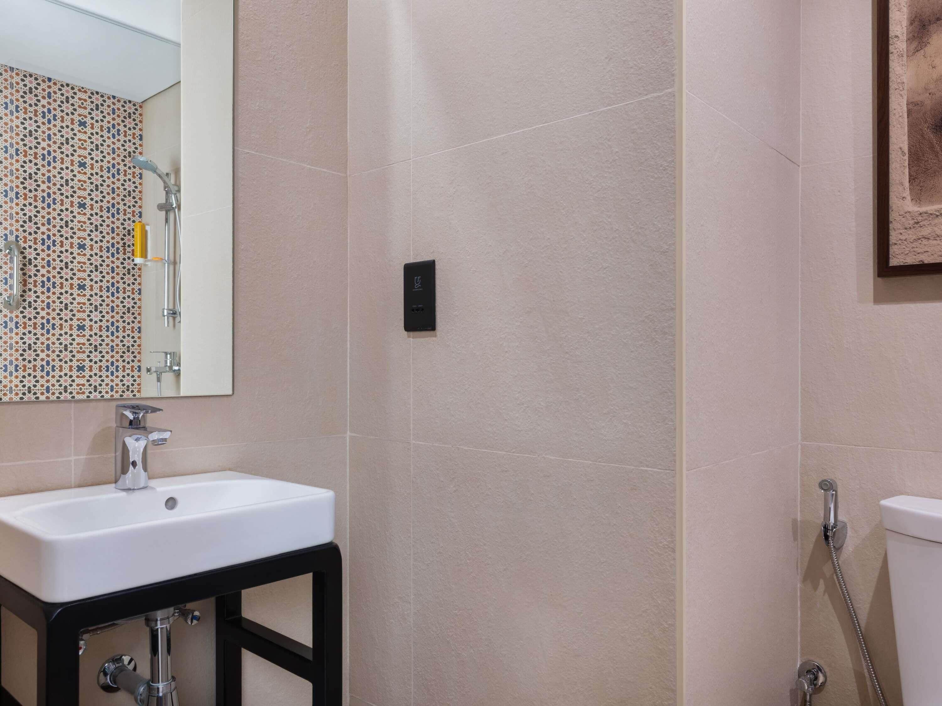 A bathroom with a white sink, a mirror, a shower, and a tiled wall.