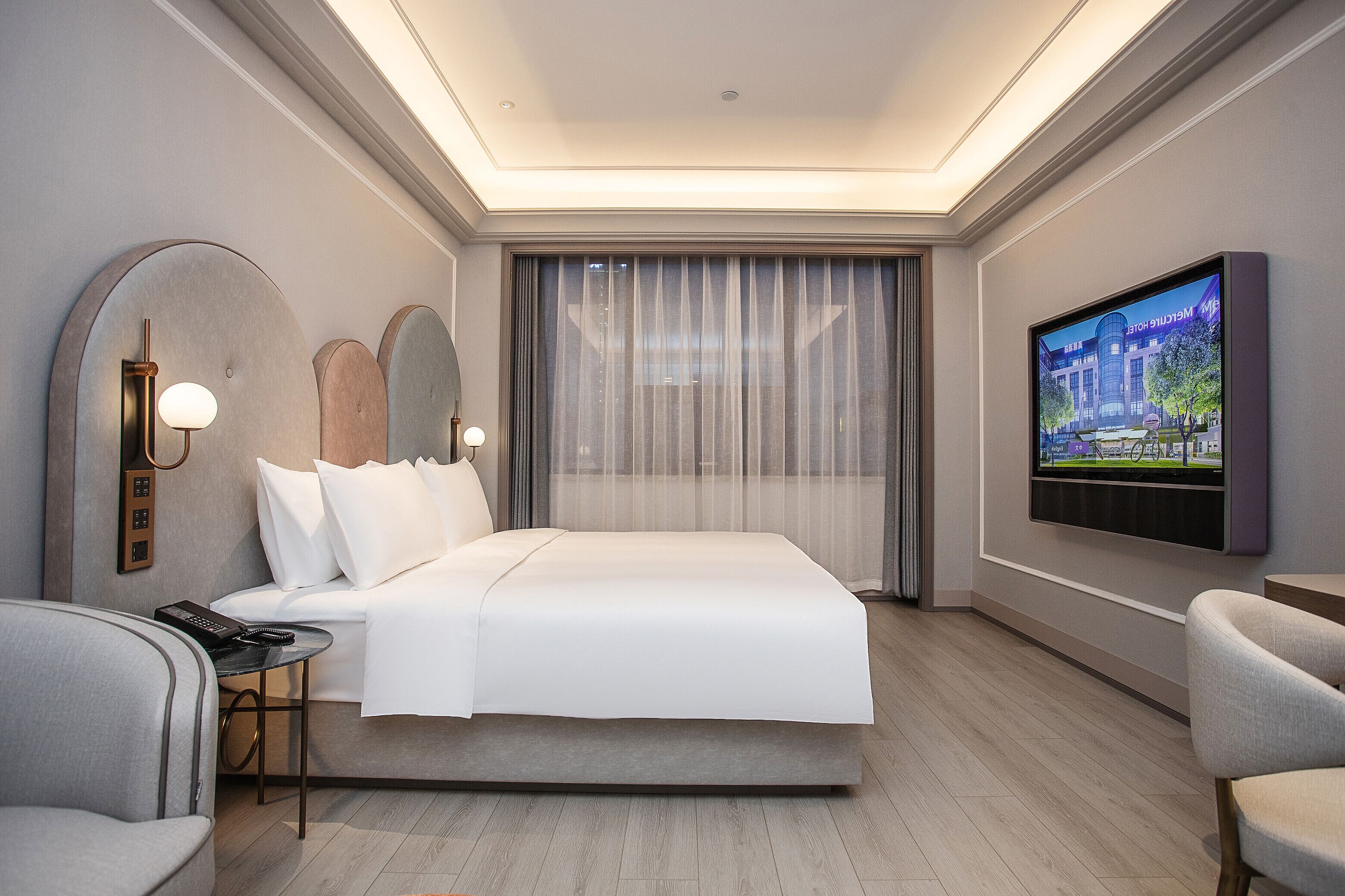 A modern hotel room with a large bed, a flat-screen TV, a desk, and a chair.