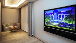 A hotel room with a sofa, a coffee table, a flat-screen TV, and a ceiling light. - Mercure Changchun Ziyou Road Dahua (Changchun)