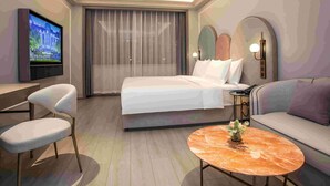 A hotel room with a bed, a TV, a desk, a chair, a sofa, and a round coffee table. - Mercure Changchun Ziyou Road Dahua (Changchun)