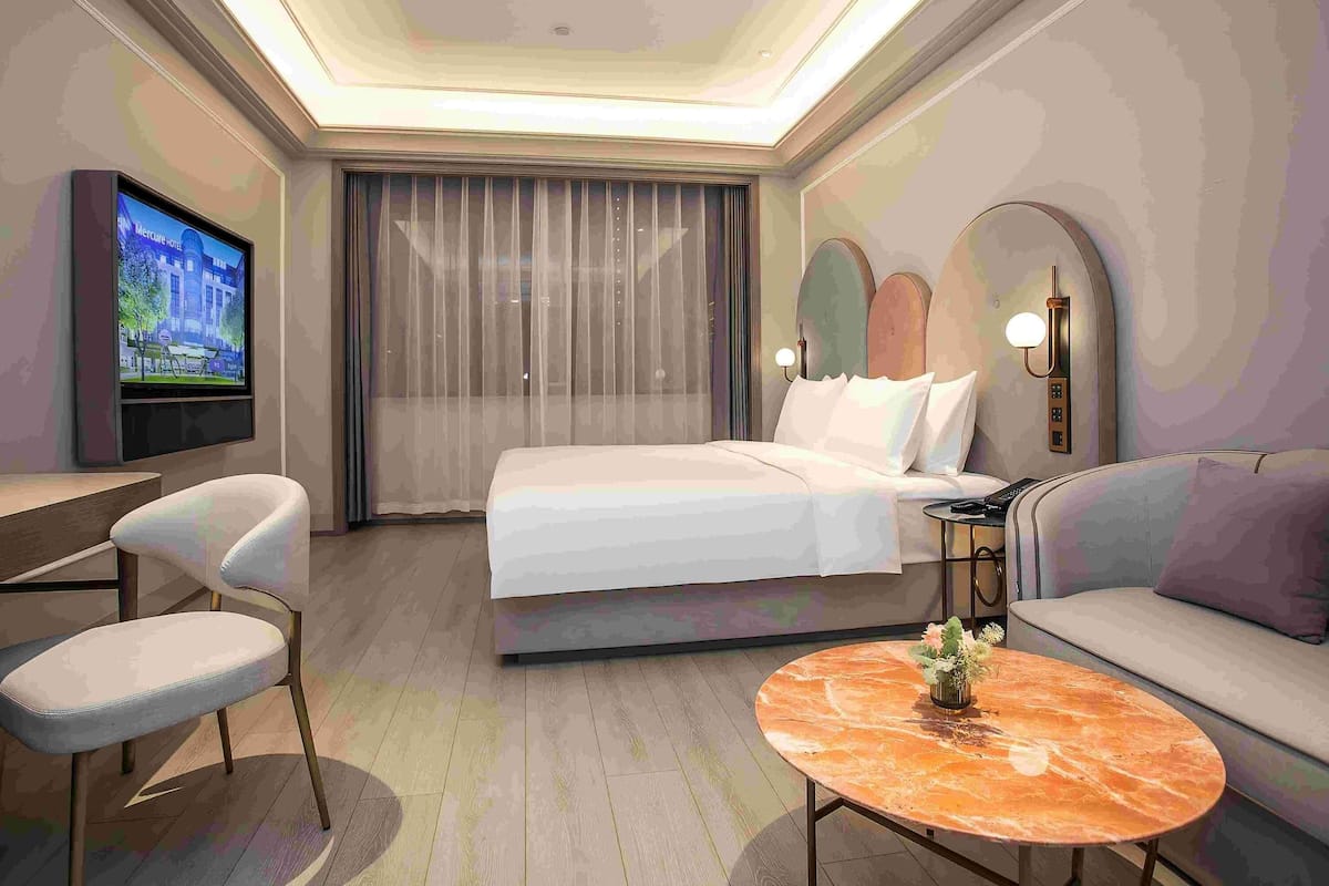 A hotel room with a bed, a TV, a desk, a chair, a sofa, and a round coffee table.