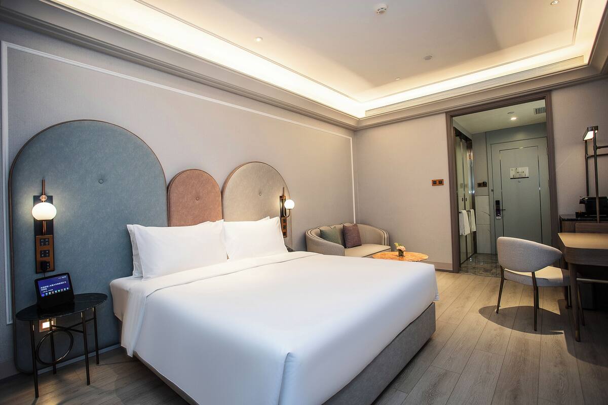 A modern hotel room with a large bed, a desk, a chair, and a small table.