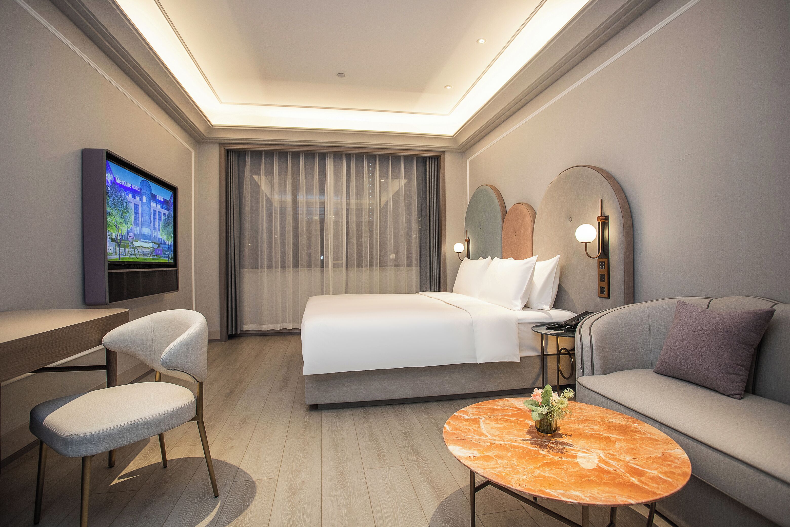 A modern hotel room with a bed, sofa, desk, and TV.