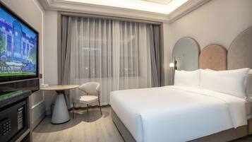 A hotel room with a large bed, a television, a small table, a chair, and a window with curtains.