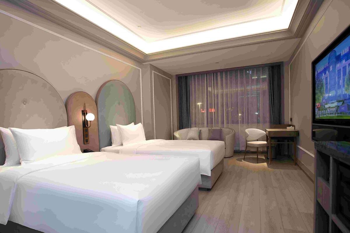 A modern hotel room with a large bed, a desk, a chair, and a television.