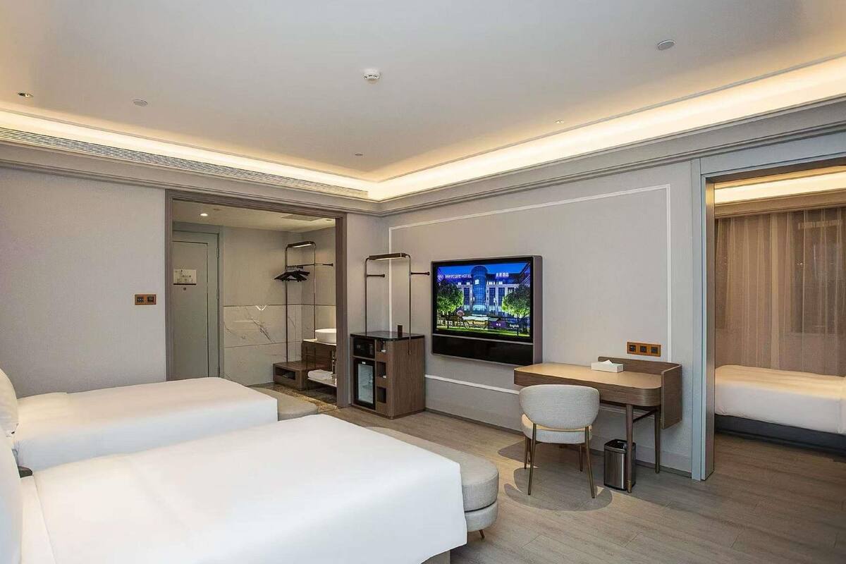 A hotel room with two beds, a desk, a TV, and a shower area.