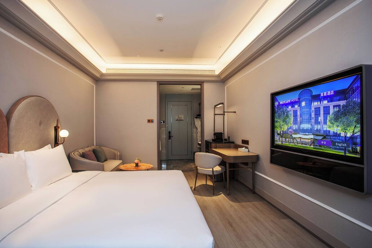 A hotel room with a bed, a desk, a chair, a television, and a door leading to another room.