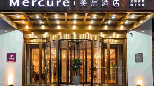 A hotel entrance with a revolving door, illuminated signage, and a potted plant in the center. - Mercure Changchun Ziyou Road Dahua (Changchun)