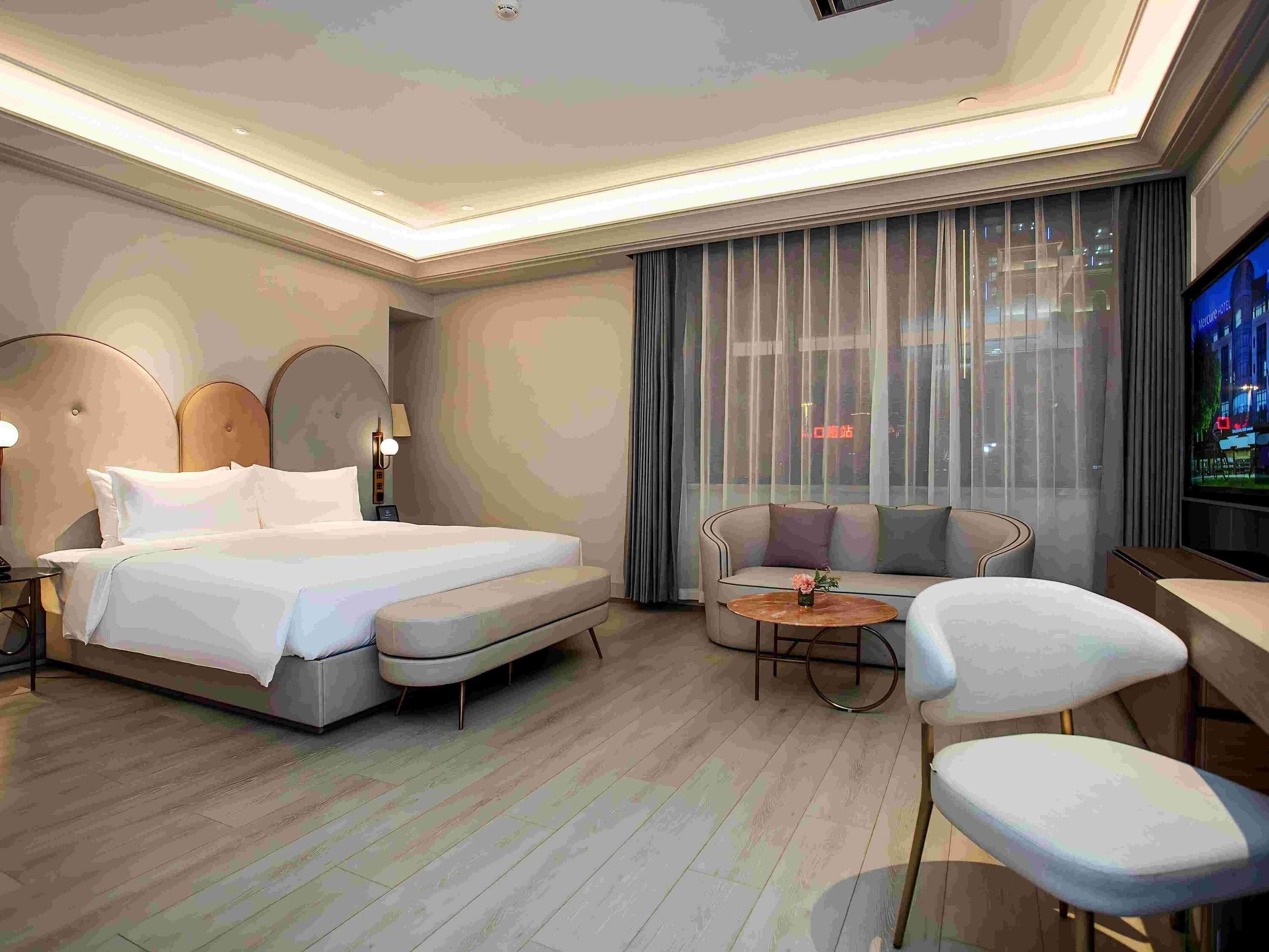 A modern hotel room with a large bed, a sofa, a small table, and a TV.