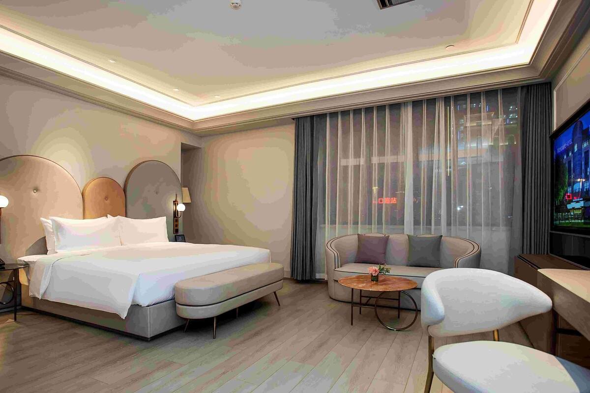 A modern hotel room with a large bed, a sofa, a small table, and a TV.