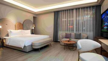 A modern hotel room with a large bed, a sofa, a small table, and a TV.