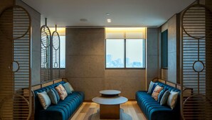 A modern living room with two blue sofas, a round coffee table, and a city view through large windows.
