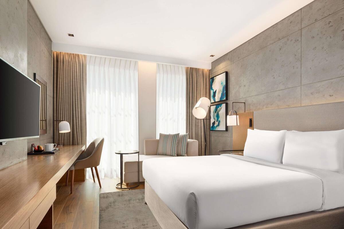 A modern hotel room with a large bed, a desk with a chair, a TV, and a small table.