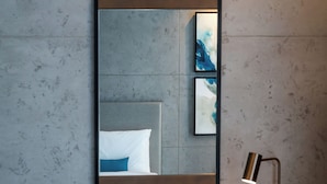A hotel room with a large mirror, a bedside table with a lamp, a kettle, and a coffee maker.