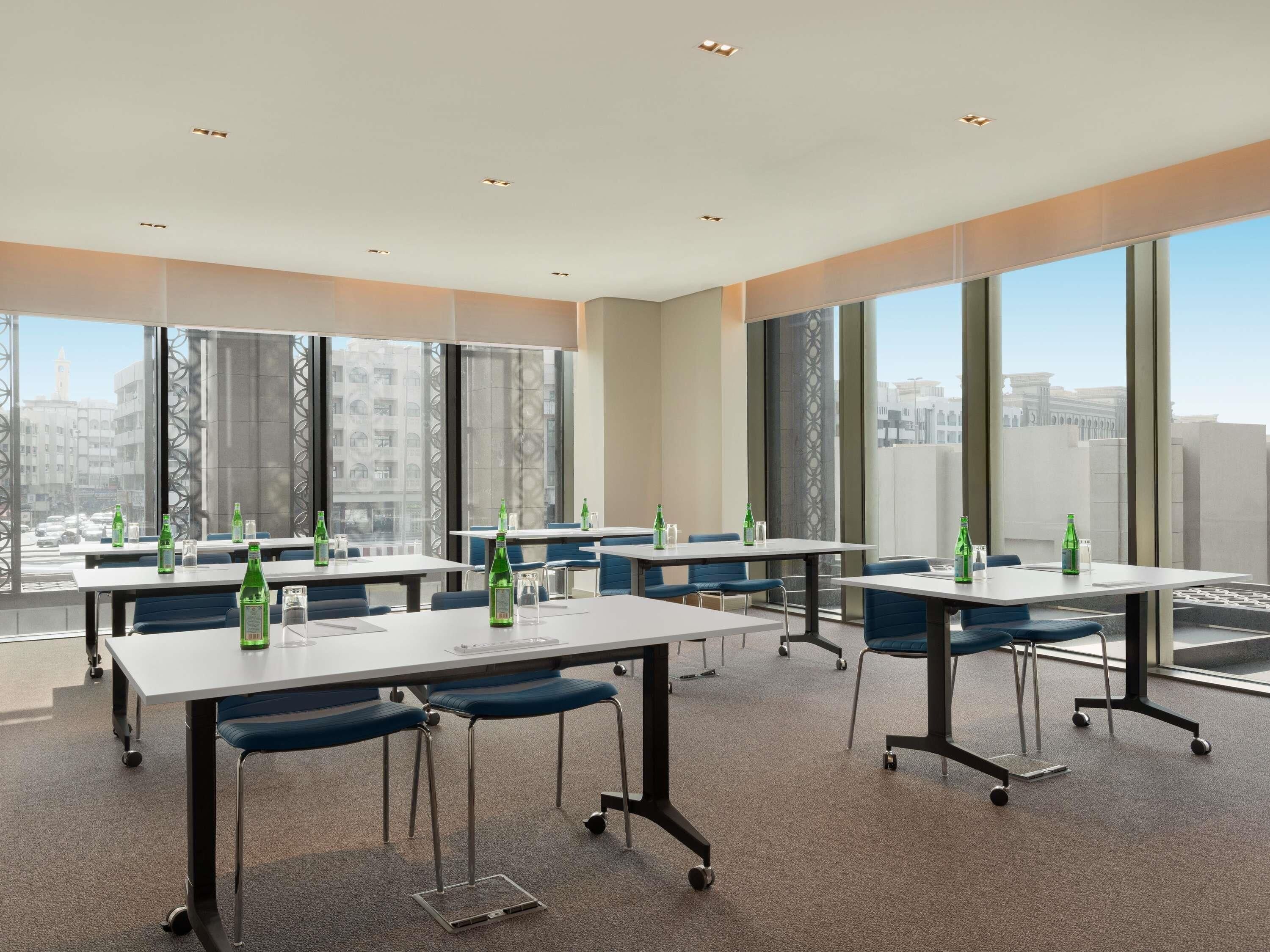 A modern conference room with large windows, tables with chairs, and bottles of water.