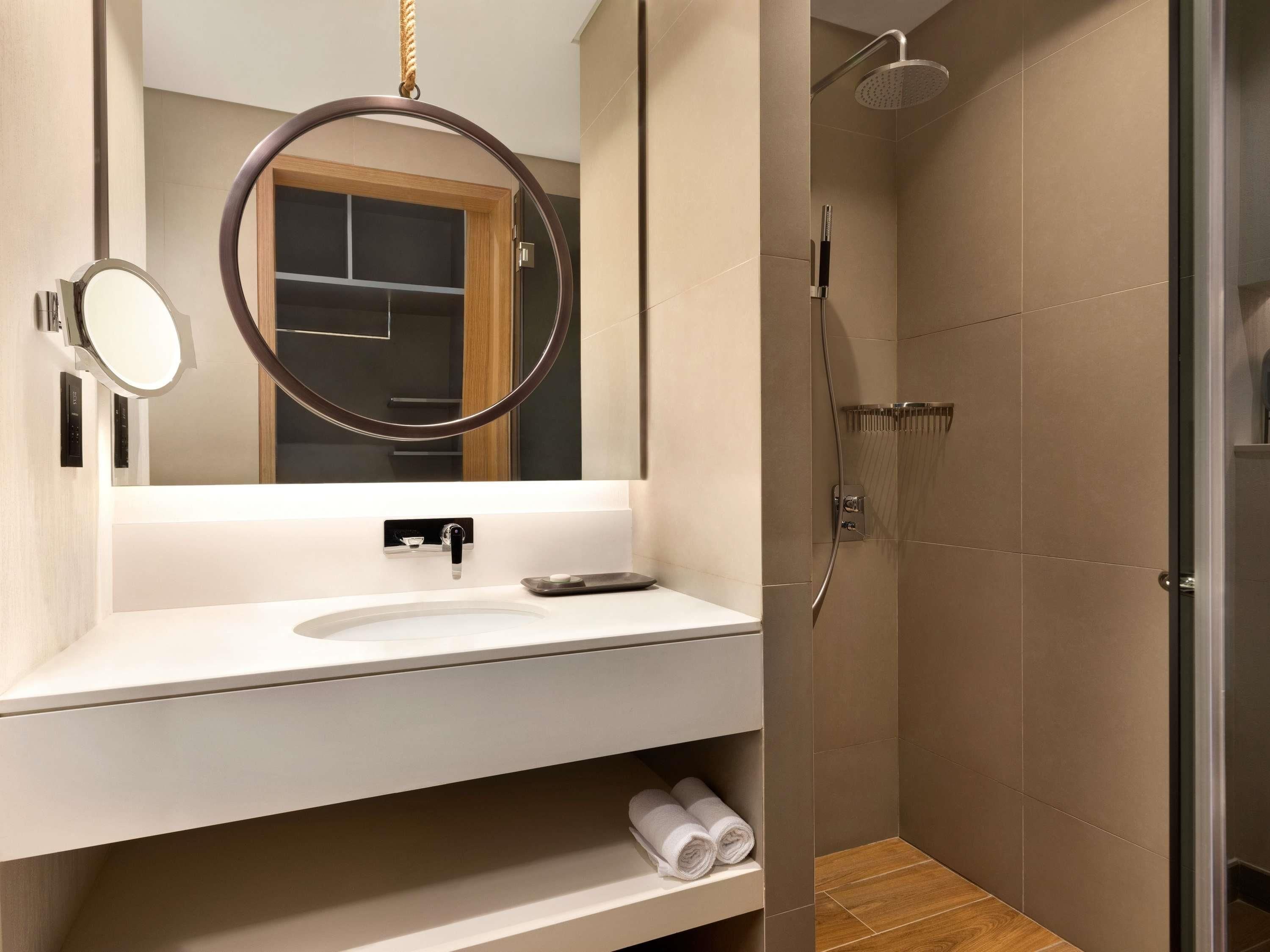 A modern bathroom with a large mirror, a sink, a shower, and a towel rack.