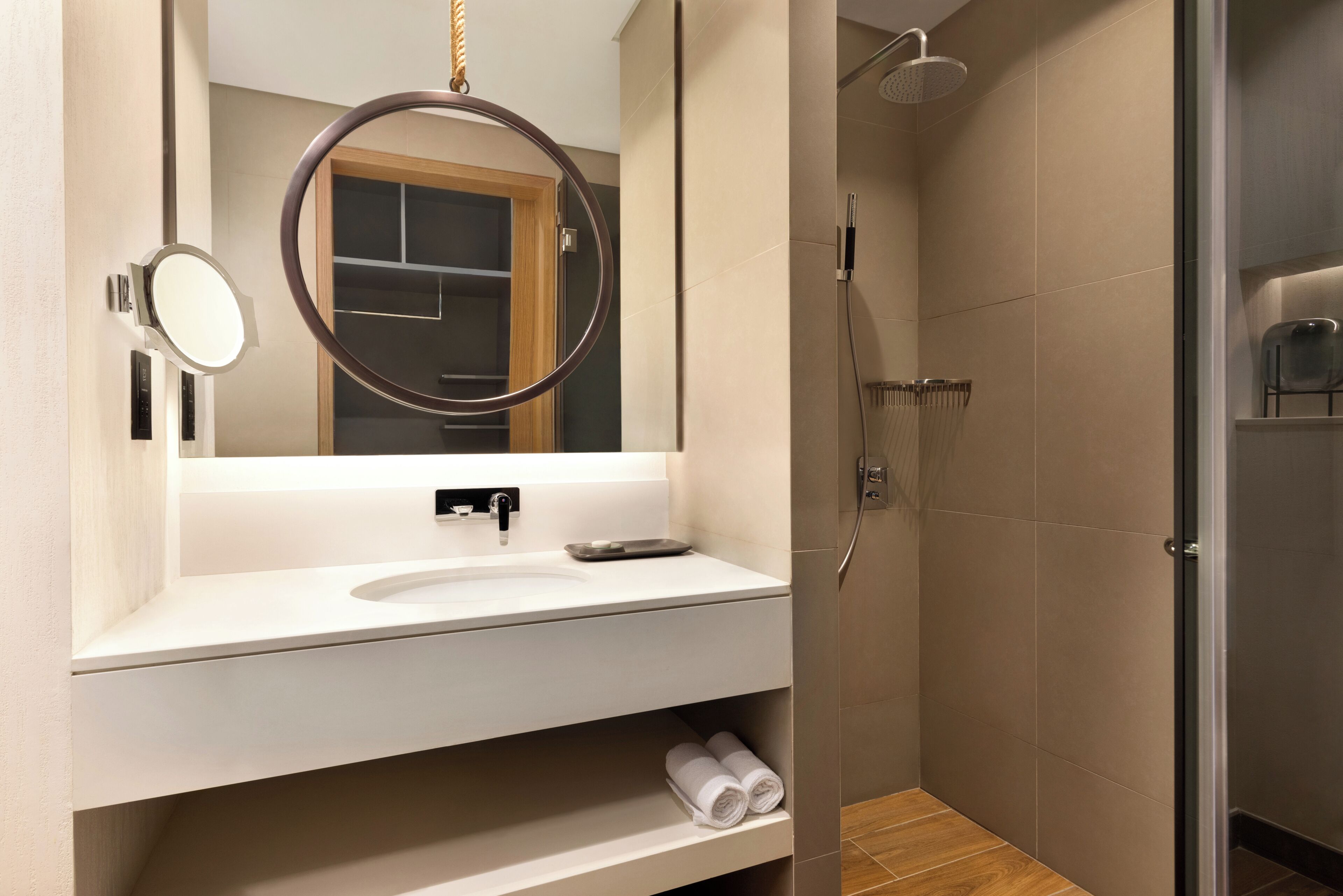 Une salle de bain moderne avec un lavabo blanc, un miroir rond, une douche et une porte en verre.