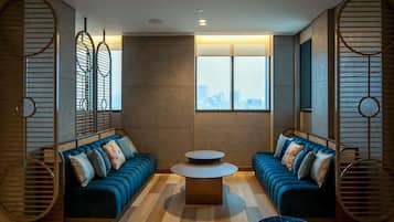 A modern living room with two blue sofas, a round coffee table, and a city view through large windows.
