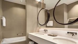 A modern bathroom with a bathtub, two sinks, and a large mirror with a circular frame.