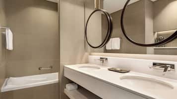 A modern bathroom with a bathtub, two sinks, and a large mirror with a circular frame.