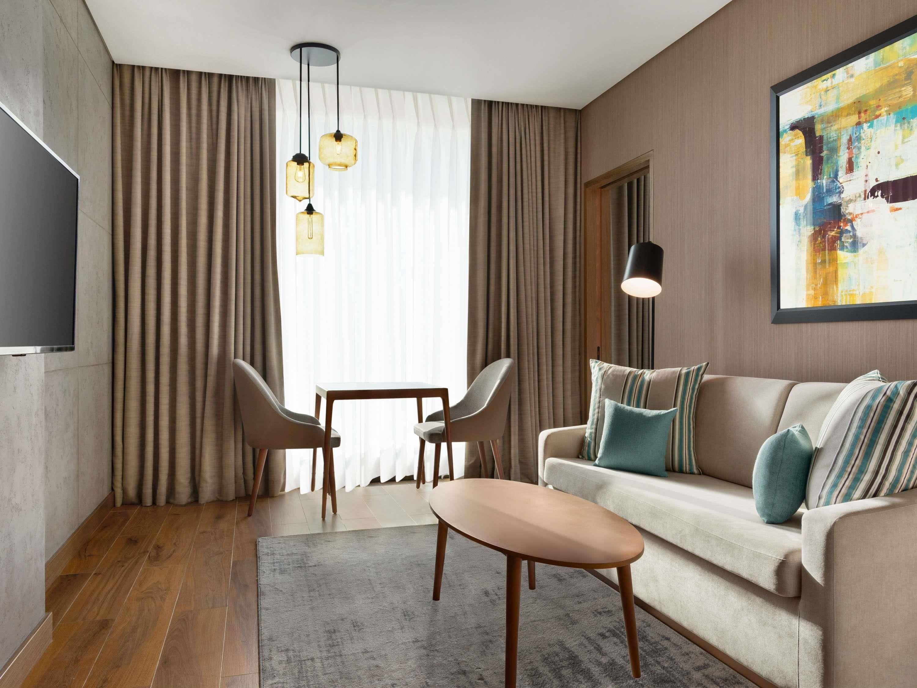 A modern living room with a sofa, two chairs, a coffee table, a TV, and a painting on the wall.