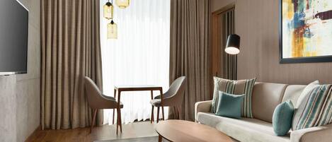 Una sala de estar moderna con un sofá, dos sillones, una mesa de centro, un televisor y un cuadro en la pared.