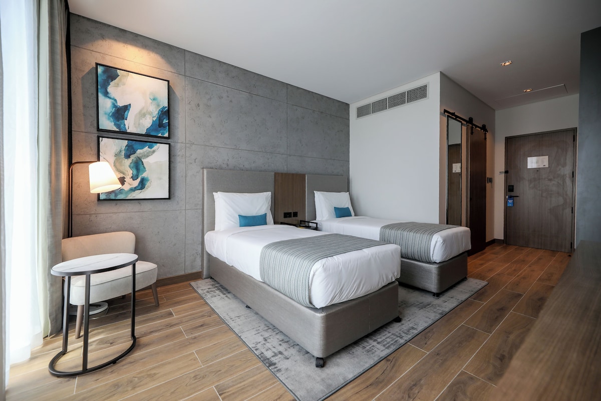 A modern hotel room with two beds, a small table, and artwork on the wall.