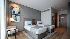 A modern hotel room with two beds, a small table, and artwork on the wall.