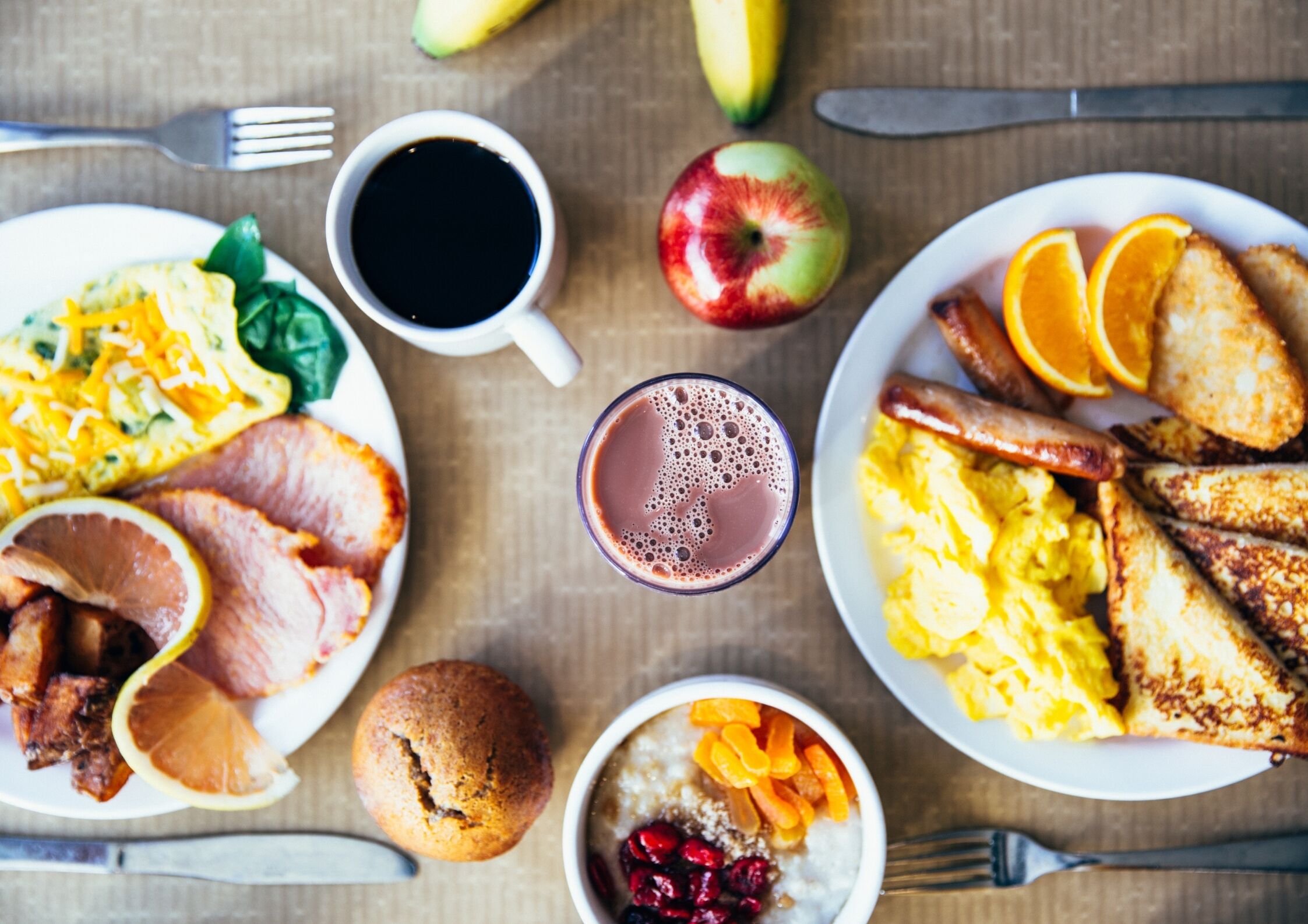 Un assortiment de plats pour le petit-déjeuner, une tasse de café et un verre de jus de fruits, le tout disposé sur une table en bois.