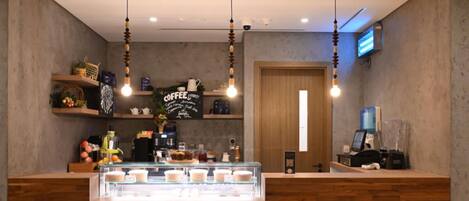 Interior de una cafetería con mostrador de madera, luces colgantes y un letrero de café en la pared.