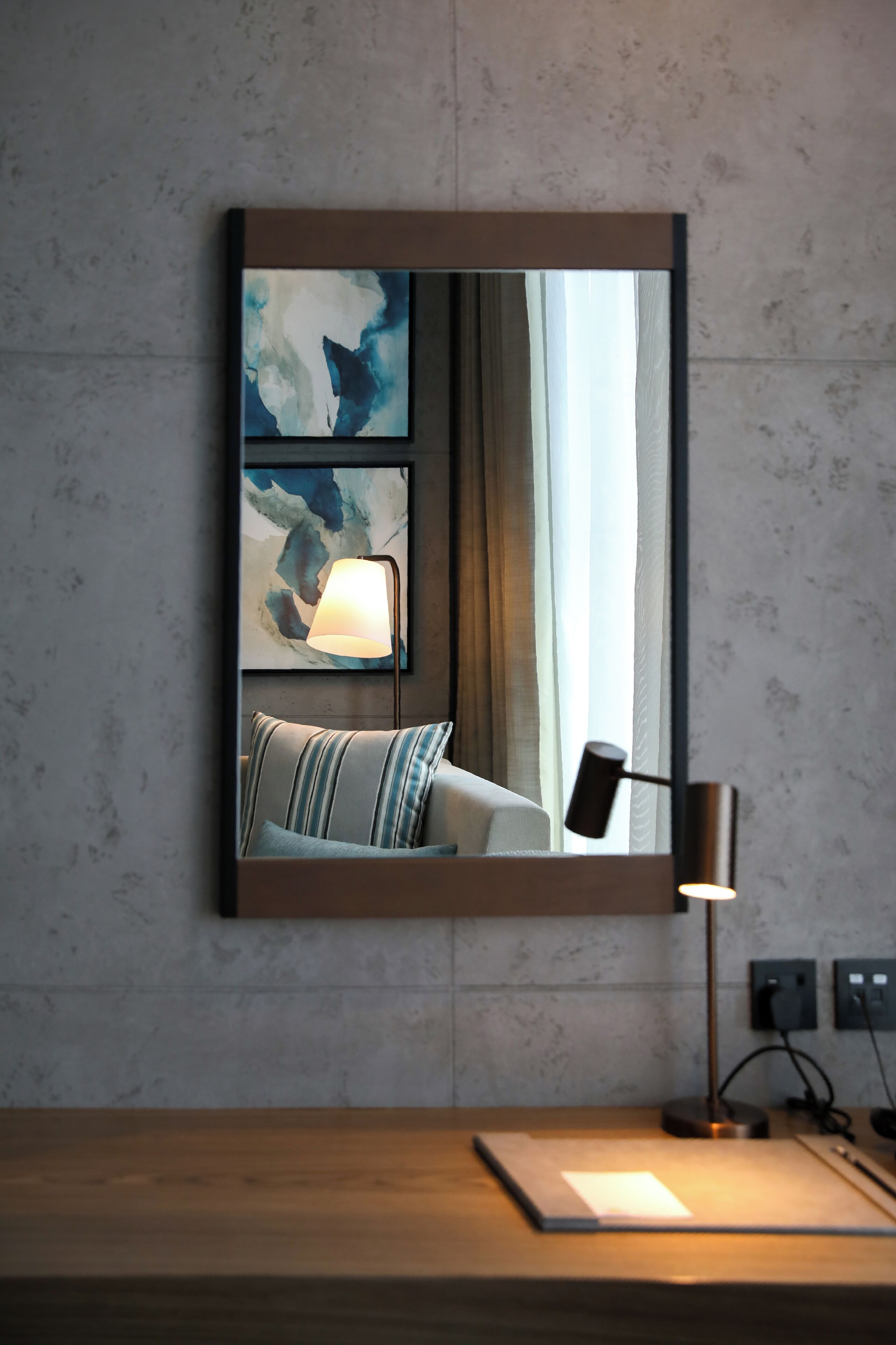 A modern hotel room with a large mirror reflecting a bed, a lamp, and abstract wall art.