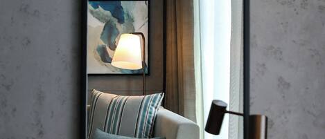 A modern hotel room with a large mirror reflecting a bed, a lamp, and abstract wall art.