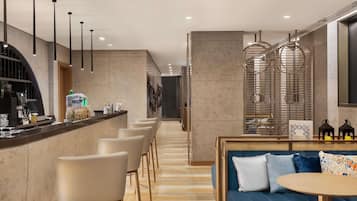 A modern hotel lobby with a bar area, seating, and a staircase.
