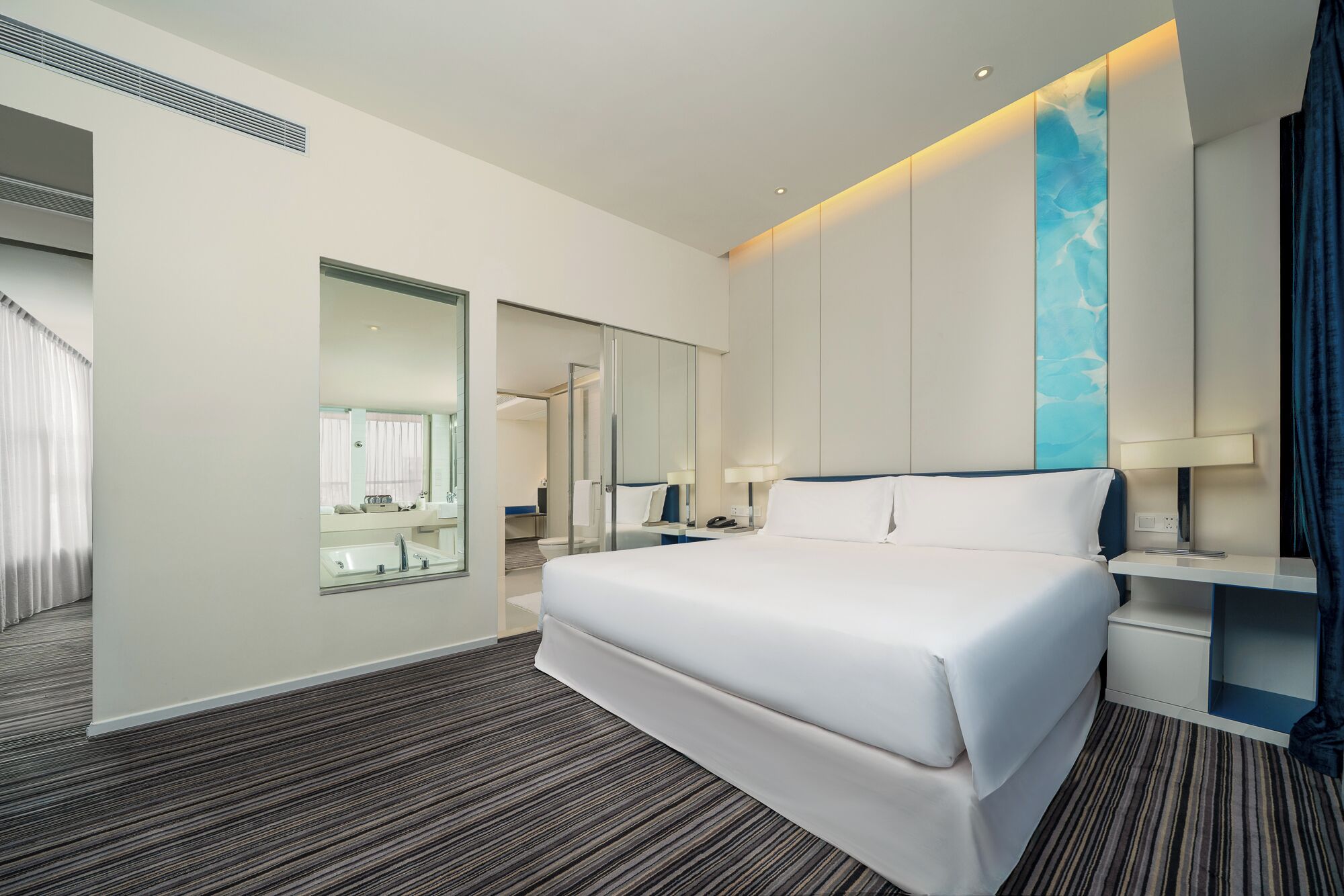 Una habitación de hotel moderna con una cama grande, un baño con espejo y vistas a la ciudad.