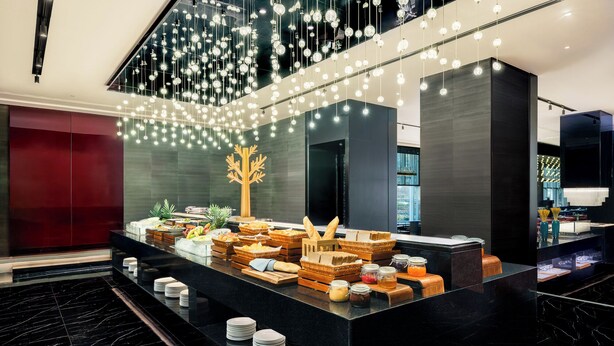 Een moderne hotel lobby met een marmeren vloer, een receptiebalie met ontbijtartikelen en een decoratieve boom.