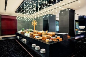 Un moderno vestíbulo de hotel con piso de mármol, una recepción con opciones de desayuno y un árbol decorativo.