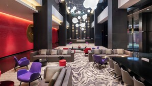 Een moderne lobby met een centraal zitgedeelte, een kamerbreed tapijt en een plafond met hangende sferische lampen.