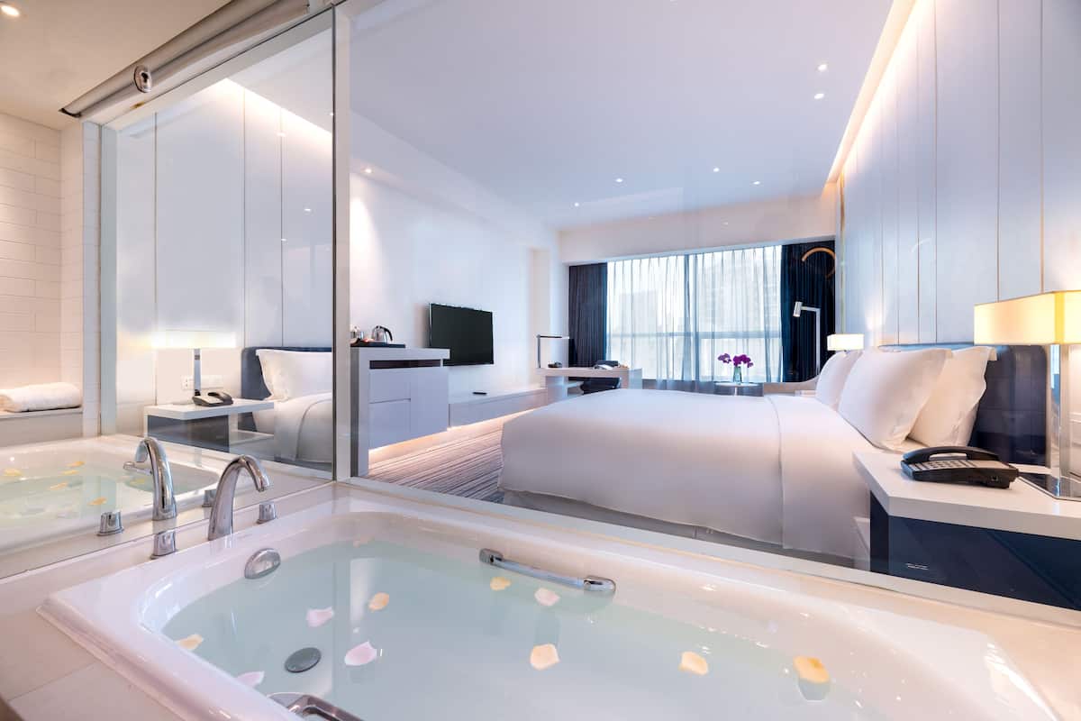 Ein modernes Hotelzimmer mit einem großen Bett, einem separaten Badezimmer mit Badewanne, einem Schreibtisch und einem Fernseher.