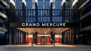 Het uiterlijk van het Grand Mercure hotel met een draaideur en een moderne glazen gevel.