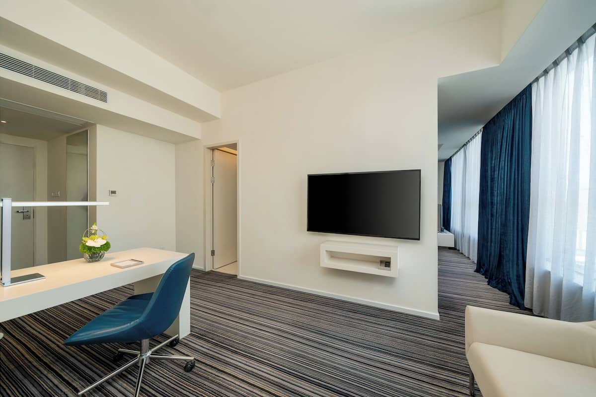 Ein Hotelzimmer mit Schreibtisch, Stuhl, Fernseher und Blick auf den Flur.