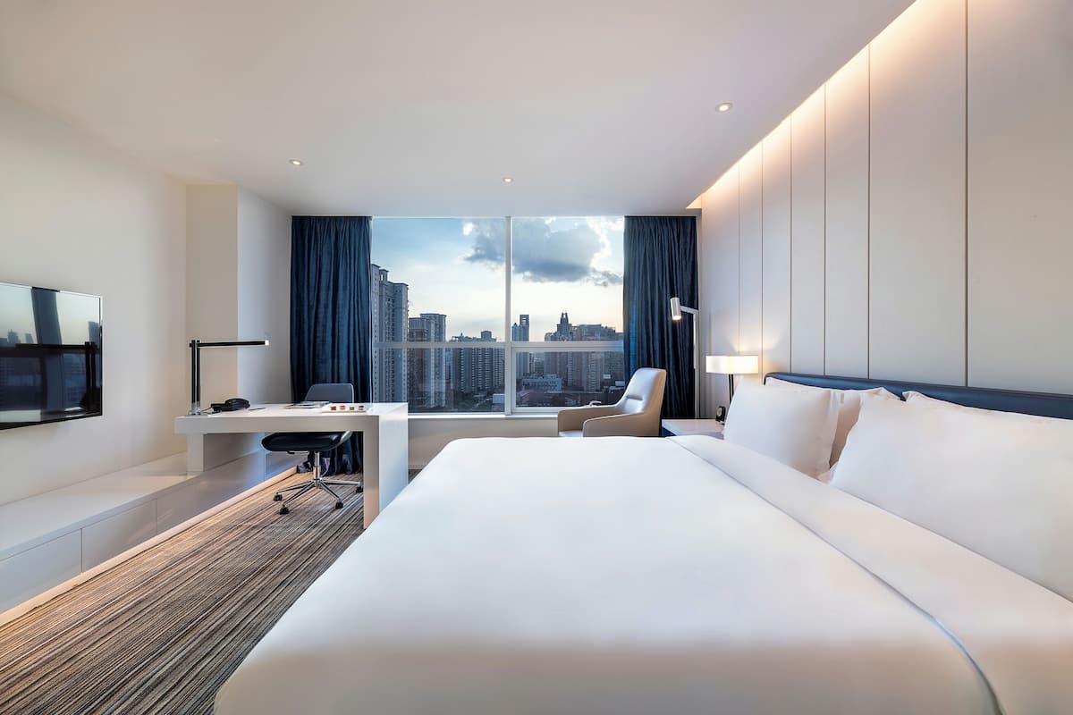 Ein modernes Hotelzimmer mit einem großen Bett, einem Schreibtisch, einem Sessel und einem Fernseher.